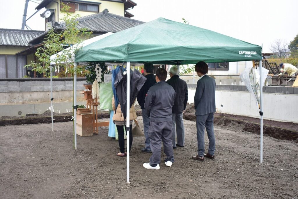 タープの下で、雨の日の地鎮祭。起立した参加者